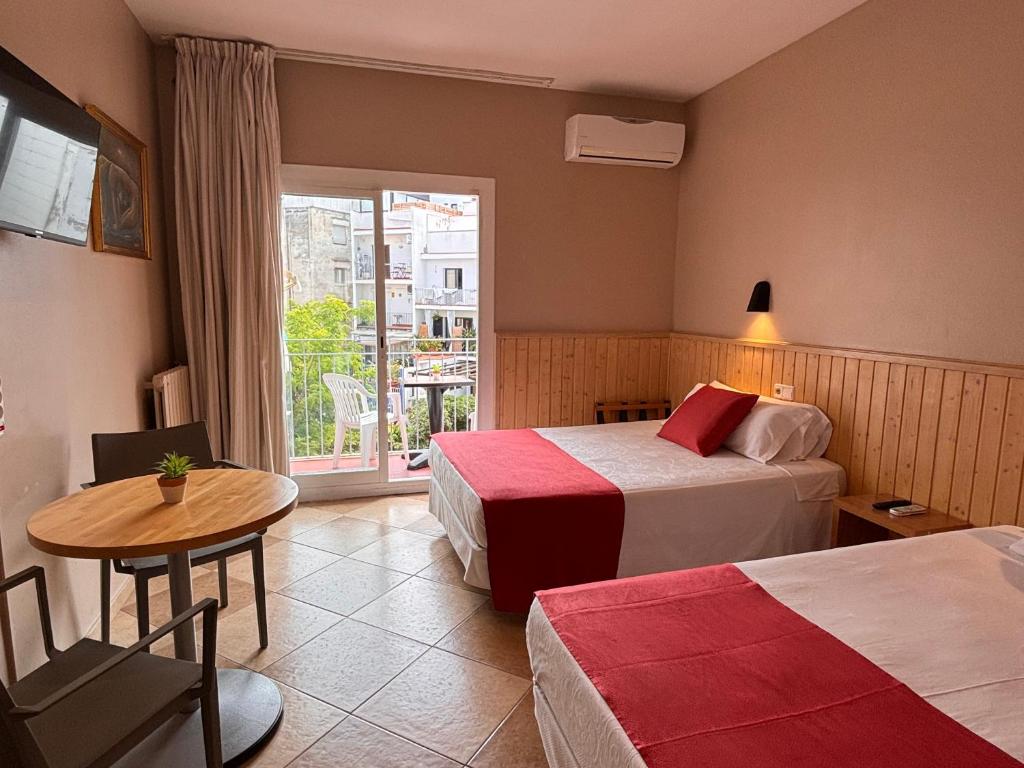 a hotel room with two beds and a table and a window at Hotel Piccadilly Sitges in Sitges