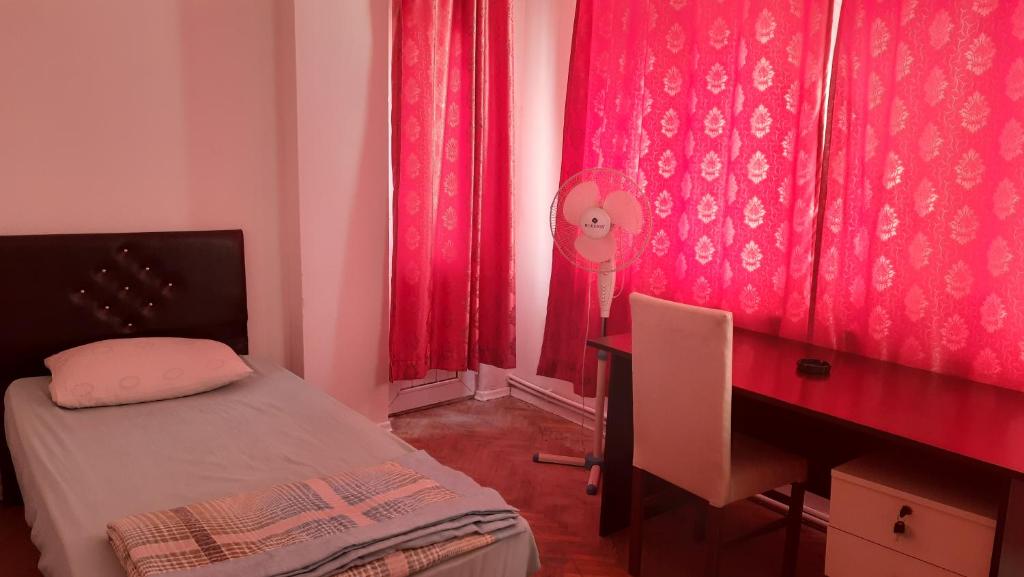 Habitación con escritorio, cama, escritorio y cortinas rojas. en Şirinevler Guest house, en Estambul