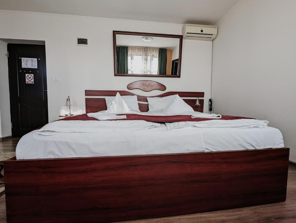Cette chambre comprend un grand lit avec des draps blancs et un miroir. dans l'établissement Conacul de pe Lac, à Şagu