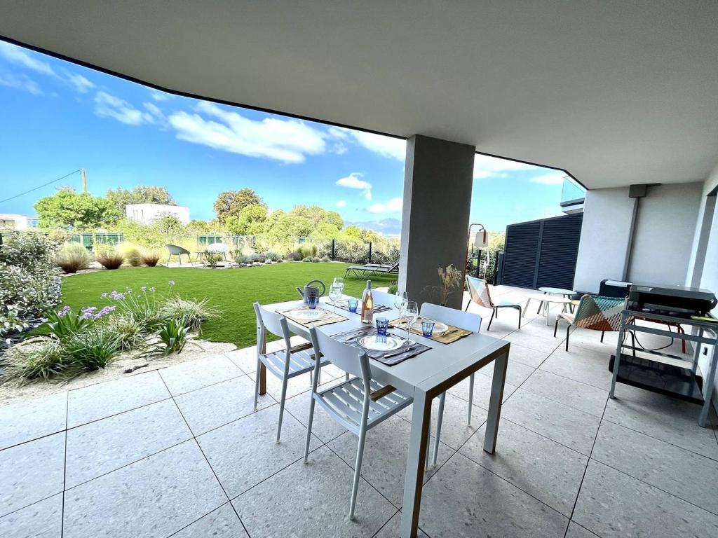 d'une terrasse avec une table, des chaises et une pelouse. dans l'établissement Appartement jardin de livia 2 rez de jardin, à Porticcio