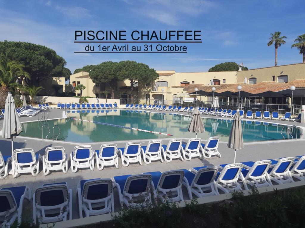 - une piscine avec des chaises et des parasols bleus et blancs dans l'établissement Studio climatisé cosy avec grande piscine chauffée, au Cap d'Agde