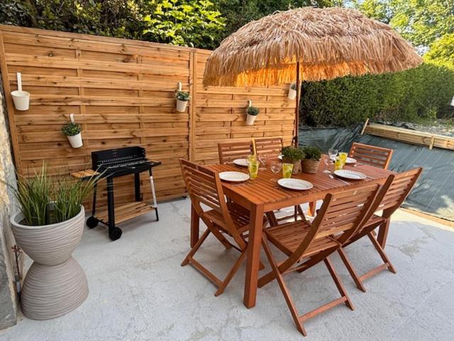 une table en bois avec des chaises, un parasol et un grill dans l'établissement Le Cottage d'Emmy - Rose, à Commes