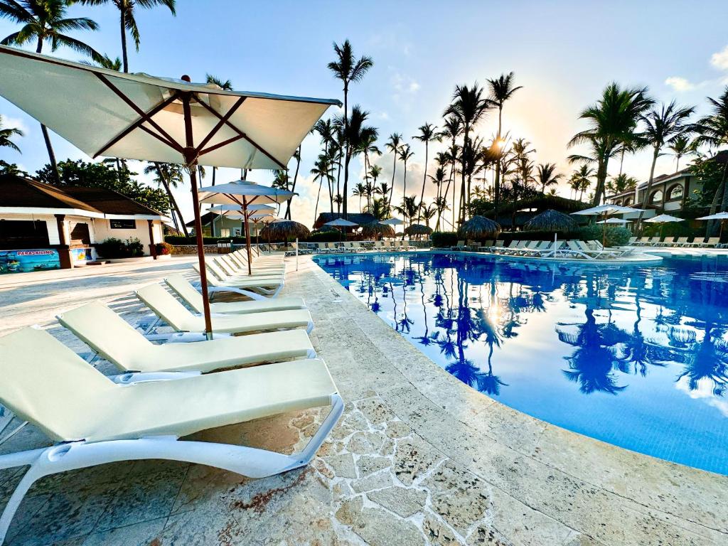 um grupo de espreguiçadeiras e um guarda-sol junto a uma piscina em Sunscape Coco Punta Cana - All Inclusive em Punta Cana