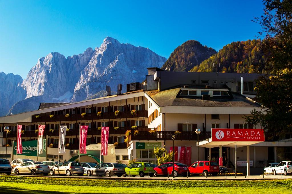 a hotel with cars parked in front of a mountain at Ramada Resort Kranjska Gora in Kranjska Gora