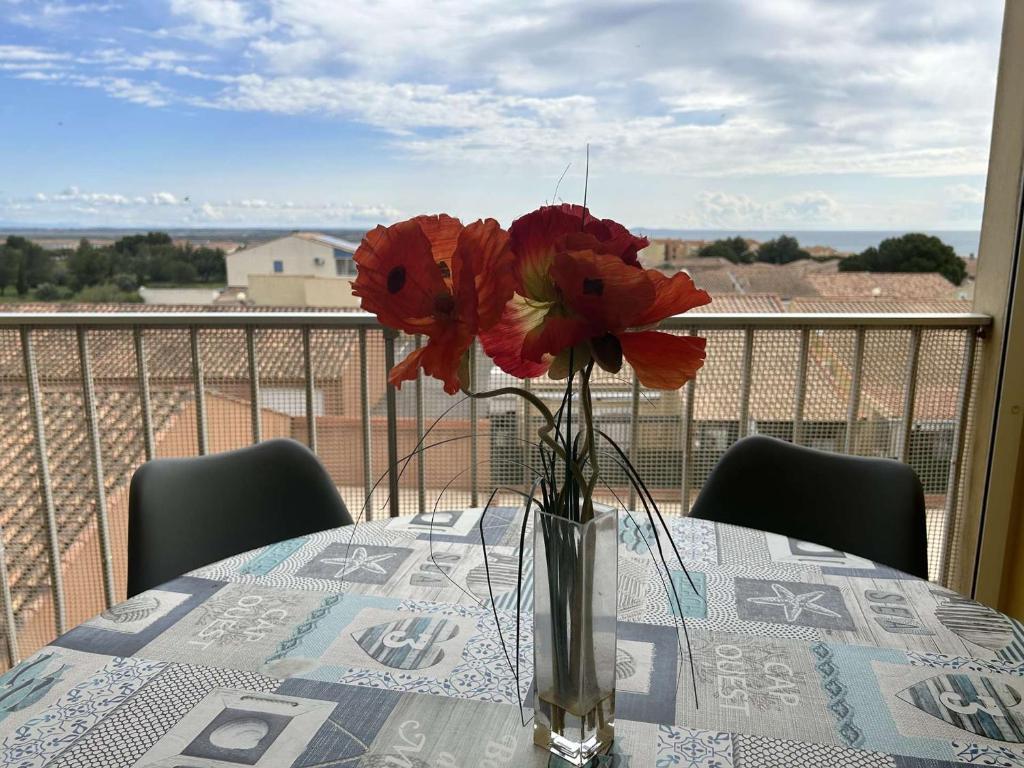 un vase avec des fleurs rouges sur une table sur un balcon dans l'établissement Charmant 2 Pièces avec Piscine, Parking Privé à 10 min de la Plage - Saint Pierre La Mer - FR-1-229D-132, à Fleury