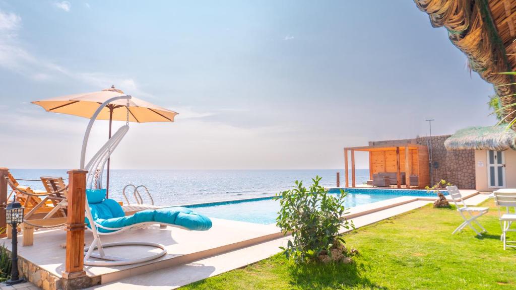 a pool with a slide and an umbrella and the ocean at Sofia - Summer Coastal Suites in Bacnotan