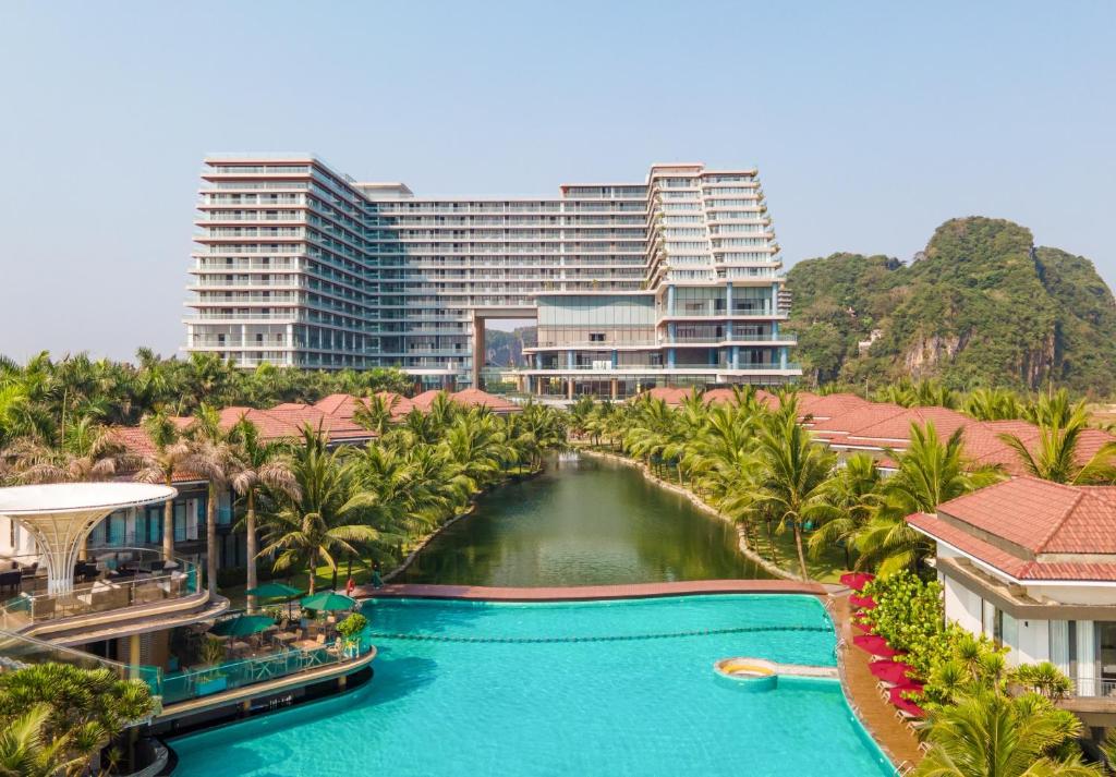 A large turquoise pool complex surrounded by palms, low red-roofed buildings and a modern resort tower.