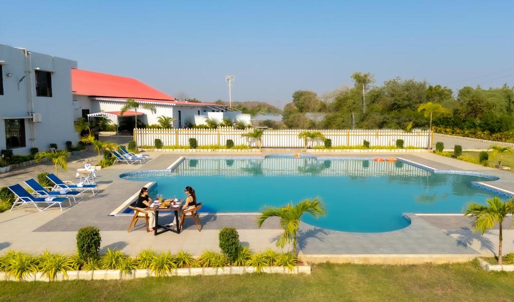 a group of people sitting at a table by a pool at Daksh Eden Greenz -A Luxury Resort in Sasan Gir in Sasan Gir