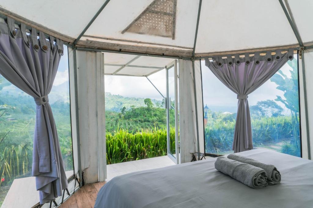 ein Schlafzimmer mit einem Bett und einem großen Fenster in der Unterkunft Alam Kita Glamping & Plantation in Munduk