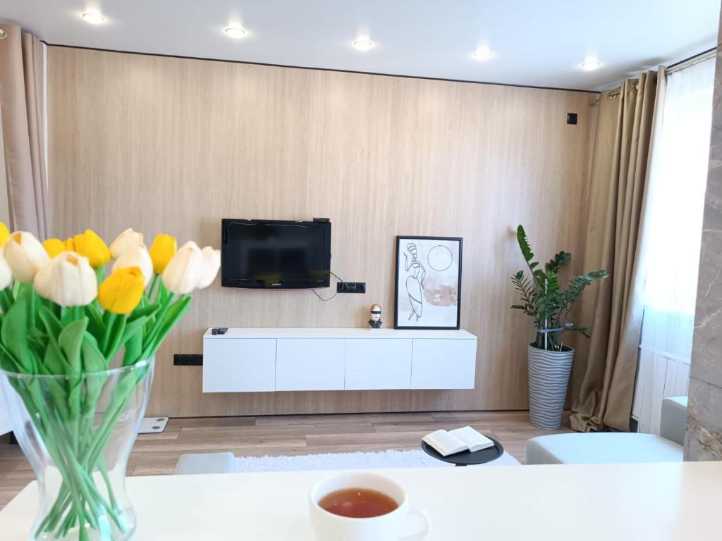 uma sala de estar com televisão e um vaso de flores em Apartament Almaty Akvarel em Almaty