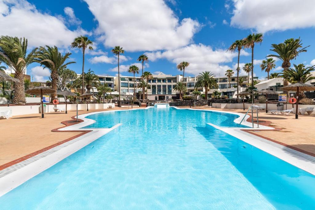 una gran piscina con palmeras y un edificio en Apartamento Rockbeach, en Costa Teguise