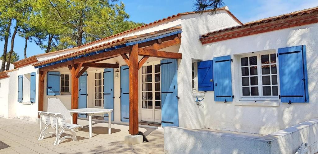 Maison blanche avec volets bleus, table et chaises dans l'établissement Maison dans les pins, à La Tranche-sur-Mer