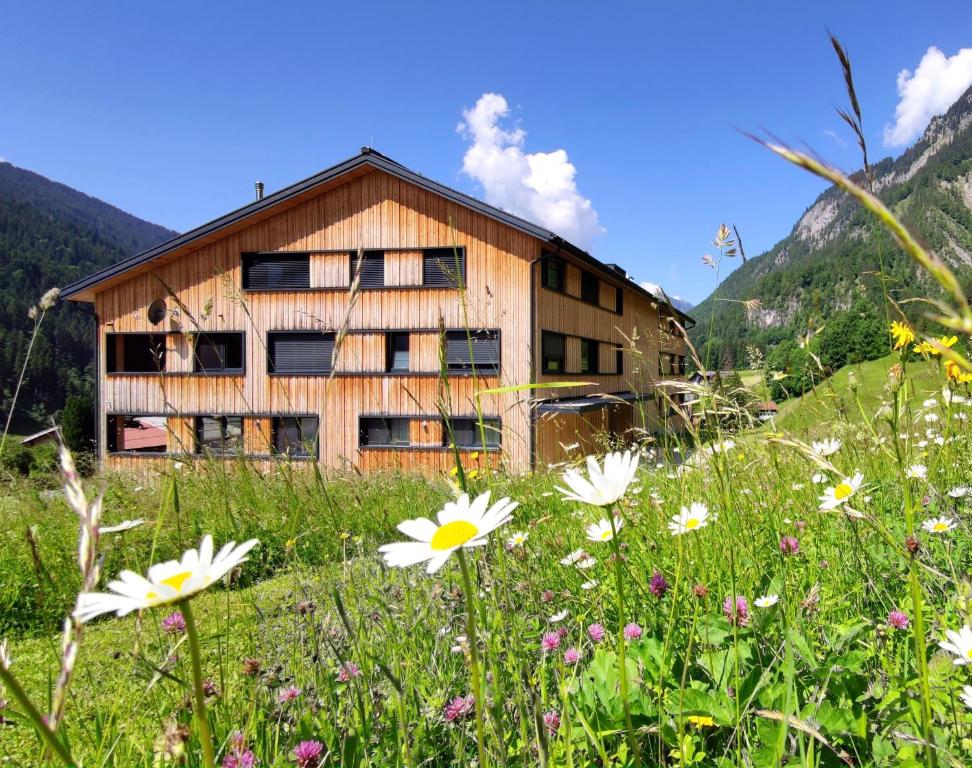 Verwall Apartment Arlberg - mit Sauna, Balkon und Gästekarte Premium في والد ام ارلبرغ: مبنى في حقل مع الزهور في الأمام