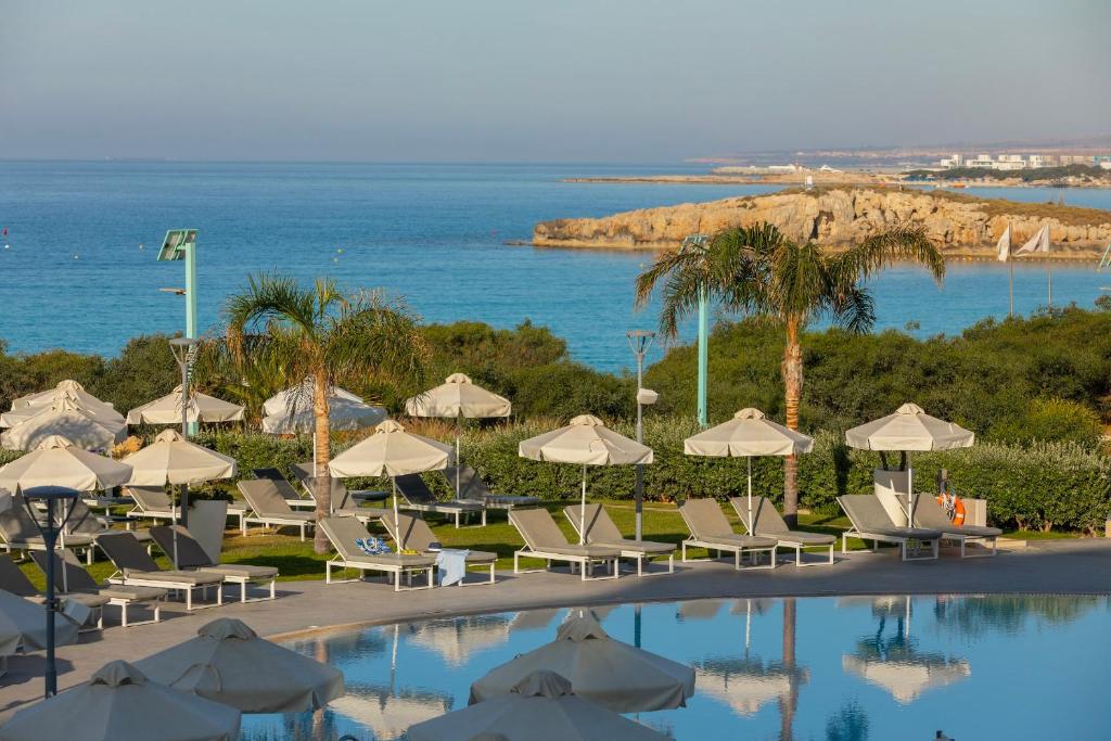 a pool with chairs and umbrellas next to the ocean at NissiBlu Beach Resort in Ayia Napa