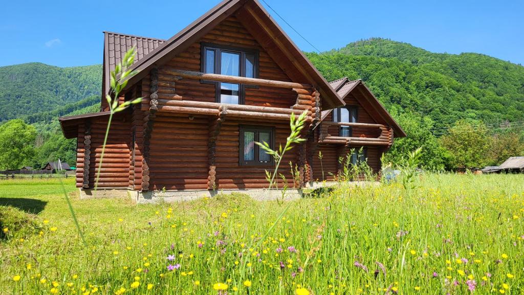 une cabane en rondins dans un champ de fleurs dans l'établissement Котеджі Карпати Fest, à Mijgiria