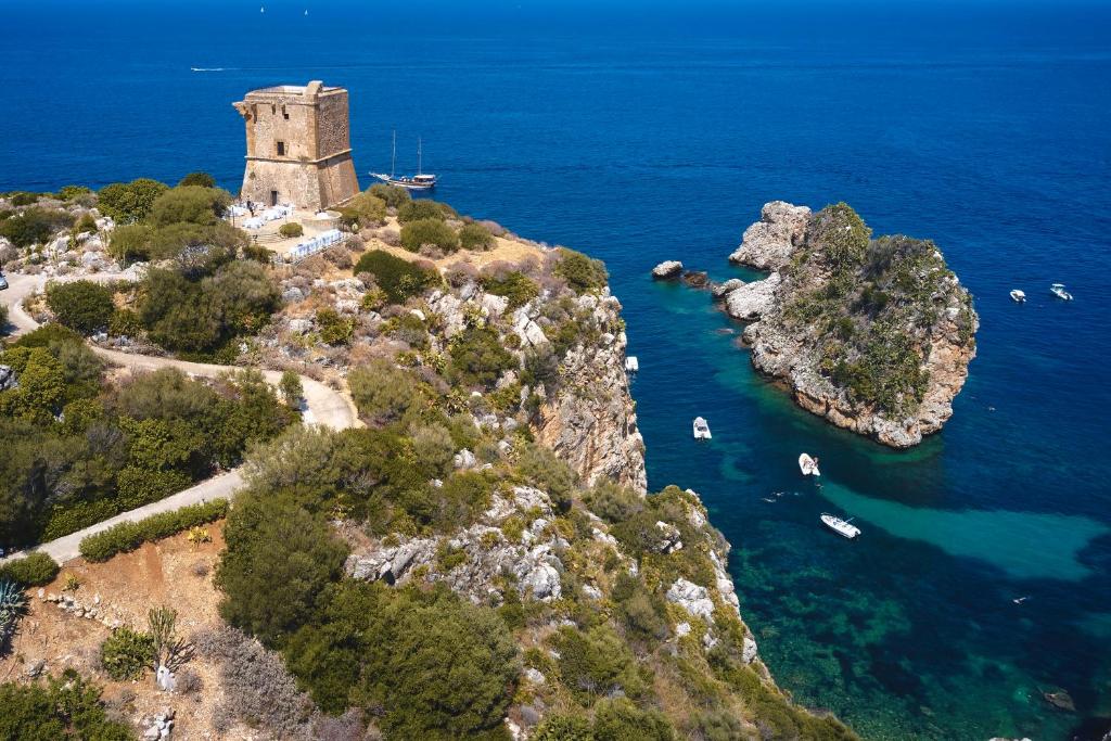 una isla con un faro y barcos en el agua en Torre di Scopello, en Scopello
