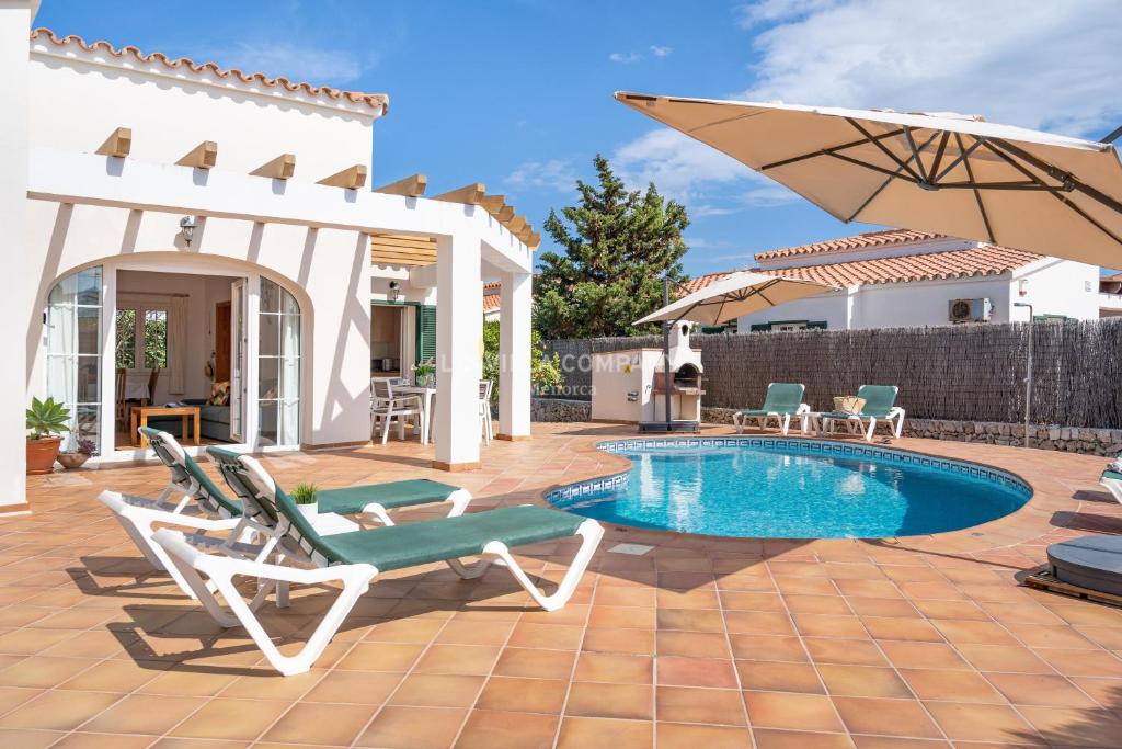 un patio con piscina, sedie e ombrellone di Villa Isabel in Cala En Porter a Cala'n Porter