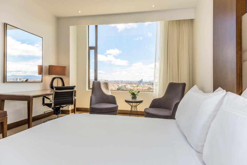 een hotelkamer met een groot bed, een bureau en stoelen bij NH Collection Bogotá Royal Teleport in Bogota