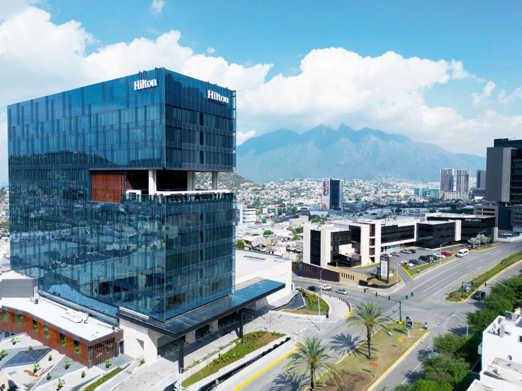 蒙特雷的住宿－Hilton Monterrey Valle，一座大玻璃建筑,位于一座有山的城市