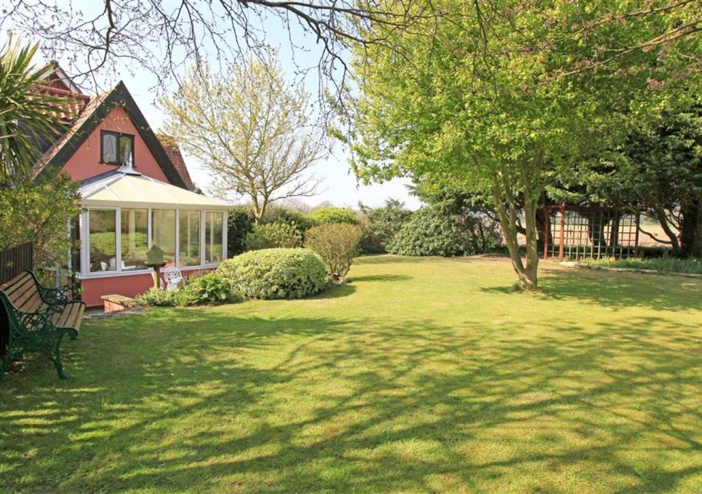 un cortile con una casa con panchina e alberi di The Cottage a Frostenden