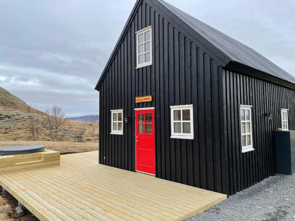 a black house with a red door and a deck at Arngrimslundur Cottages in Fludir