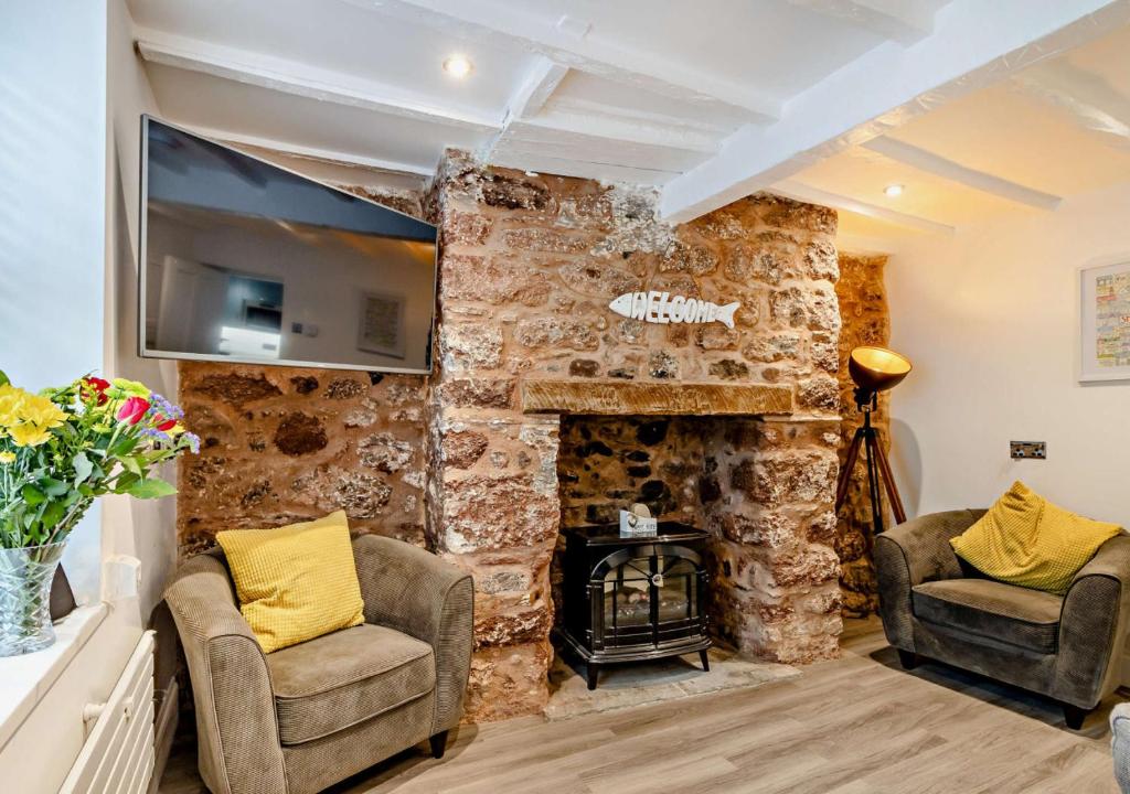 a living room with two chairs and a stone fireplace at Bilbos Cottage in Shaldon