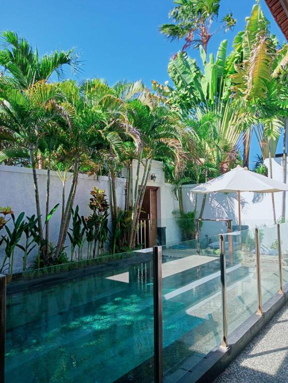 a swimming pool in front of a house with trees at Glisten Up Villa Beach Side Sanur! in Sanur