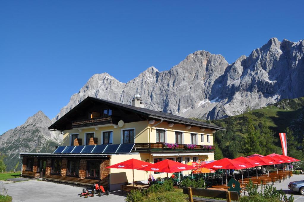 a building with red umbrellas in front of a mountain at Gasthof Hunerkogel in Ramsau am Dachstein