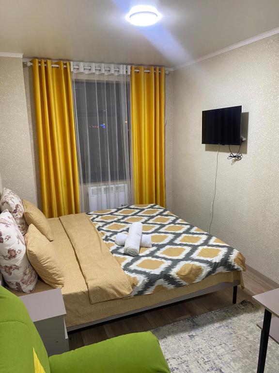 um quarto com uma cama com cortinas amarelas e uma televisão em Нарэл em Bishkek