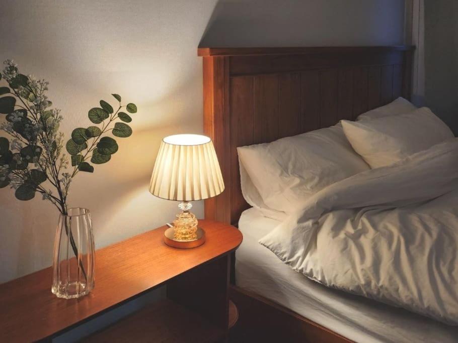 a table with a lamp and a vase of flowers next to a bed at Gwang An Stay in Busan