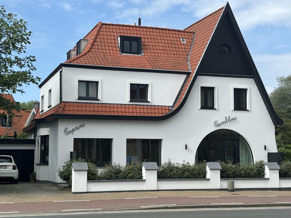 een wit huis met een rood dak bij CAPRINO Guesthouse in Knokke-Heist