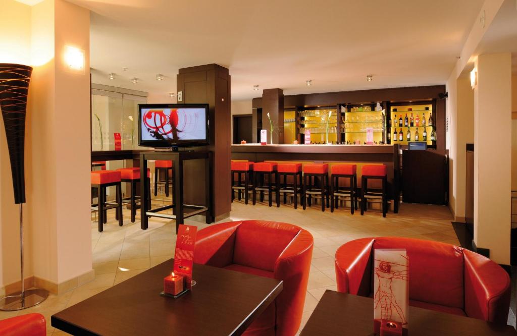 a restaurant with a bar with red chairs and a television at Leonardo Hotel München City Center in Munich
