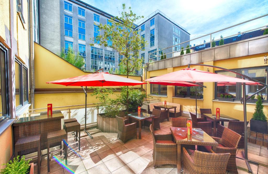 a patio with tables and chairs and umbrellas at Leonardo Hotel München City Center in Munich