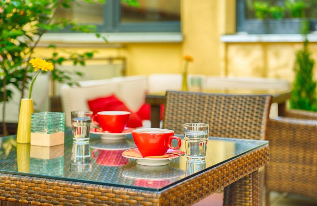 a glass table with red cups and plates on it at Leonardo Hotel München City Center in Munich