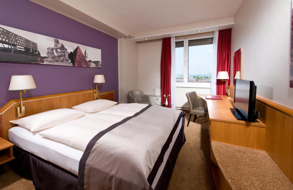 a hotel room with a bed and a desk and a television at Leonardo Hotel Karlsruhe in Karlsruhe