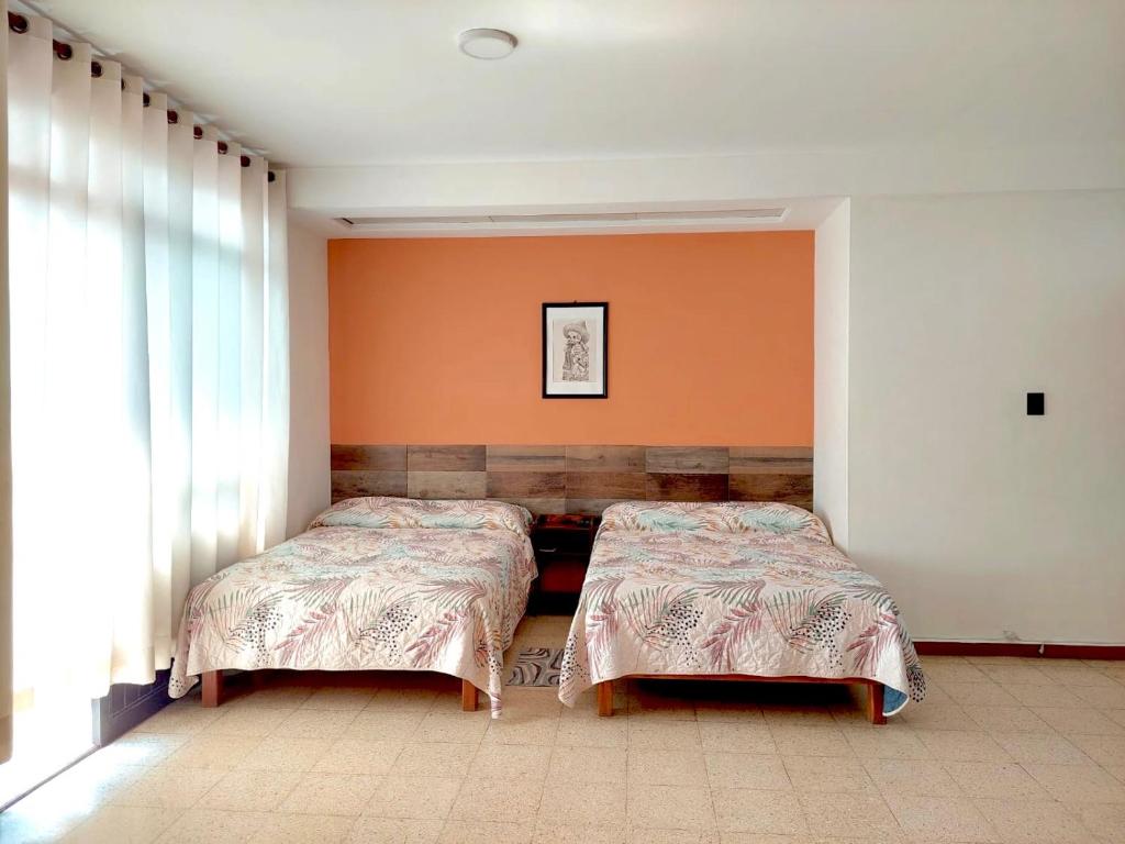 two beds in a room with orange walls at Hotel Galaxia in Oaxaca City