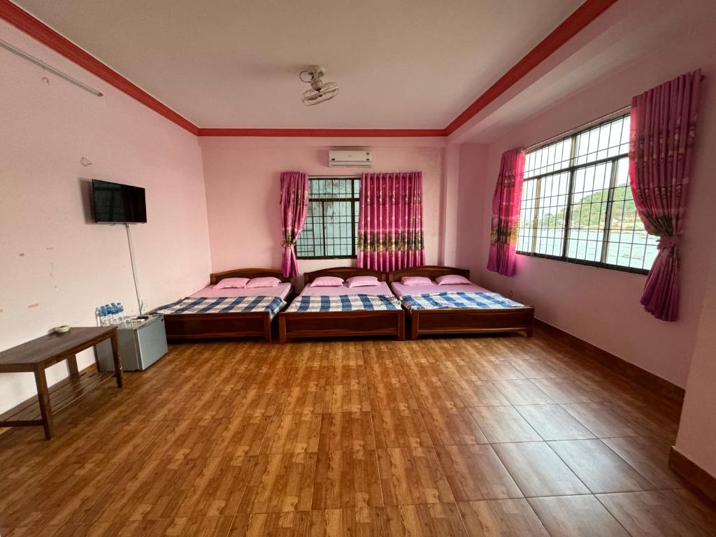 a room with two beds and a table and windows at Nhà Nghỉ M91 in Ha Tien