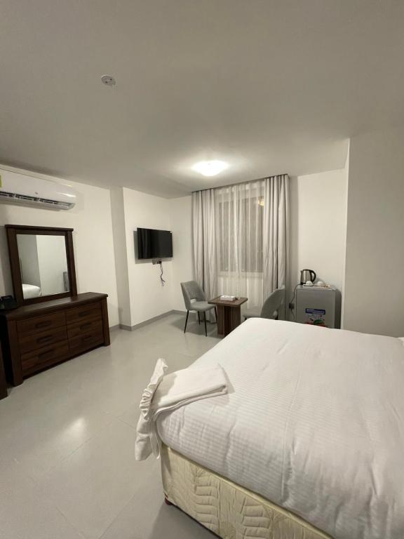 a white bedroom with a bed and a television at Iveria Hotel Apartments in Ḩayl Āl ‘Umayr