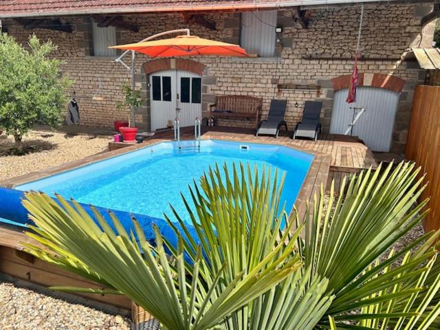 ein Pool mit Sonnenschirm und einigen Stühlen und ein Haus in der Unterkunft Gîte : La Petite Grange in Valojoulx