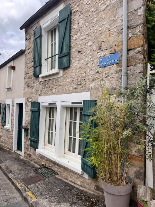 un bâtiment en pierre avec des fenêtres à volets verts et un panneau de rue dans l'établissement Charme et Calme au Cœur de ville, à Moret-sur-Loing