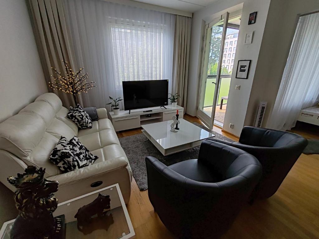 uma sala de estar com um sofá e duas cadeiras e uma televisão em Lovely apartment near the Beach em Helsinque
