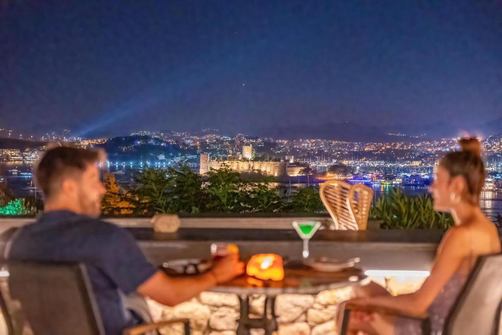 a man and woman sitting at a table looking at a city at night at Manastir Hotel & Suites in Bodrum City