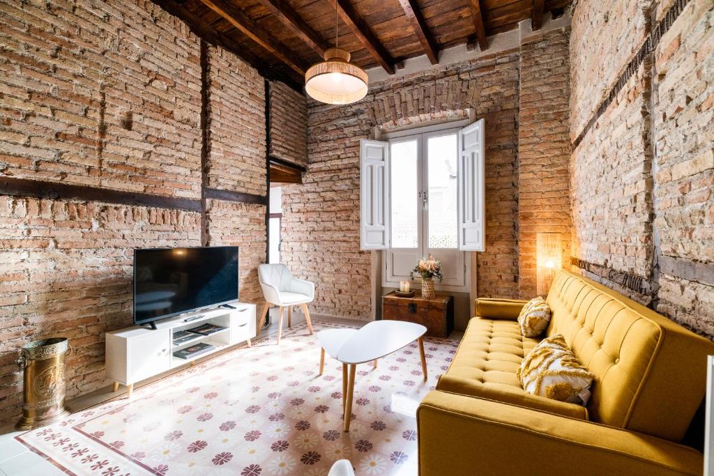 een woonkamer met een bank en een tv en een bakstenen muur bij Ma&to Alhóndiga Apart in Granada