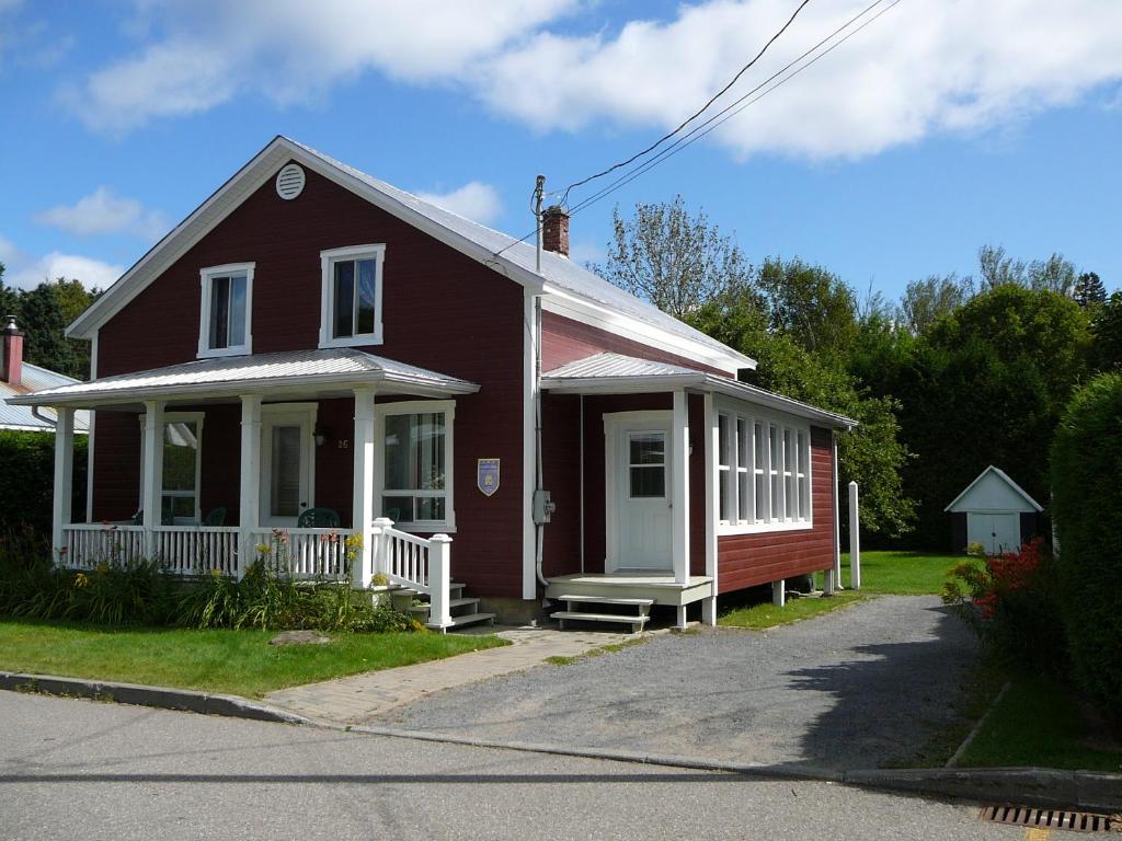 una pequeña casa roja con un porche blanco en La Maison Clarence en Baie-Saint-Paul