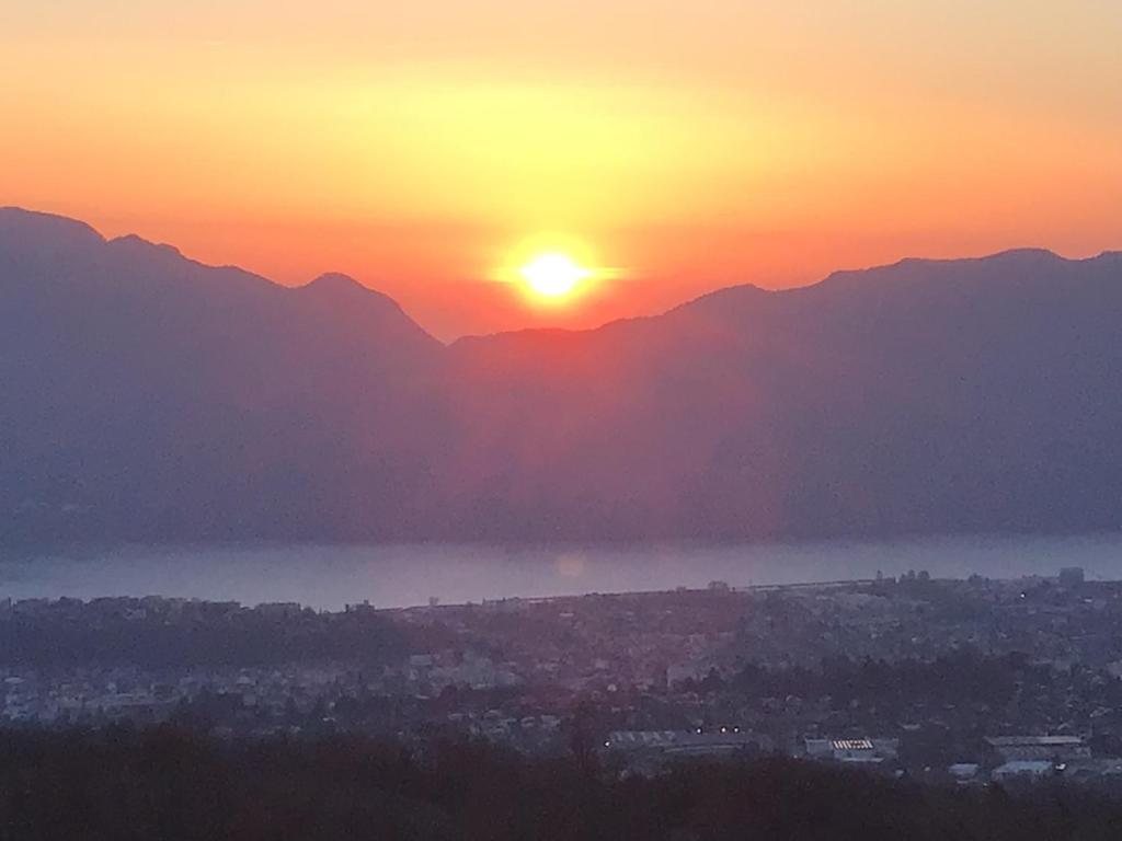 un coucher de soleil sur une ville avec des montagnes en arrière-plan dans l'établissement Appartement avec vue sur le lac du Bourget, à Pugny-Chatenod