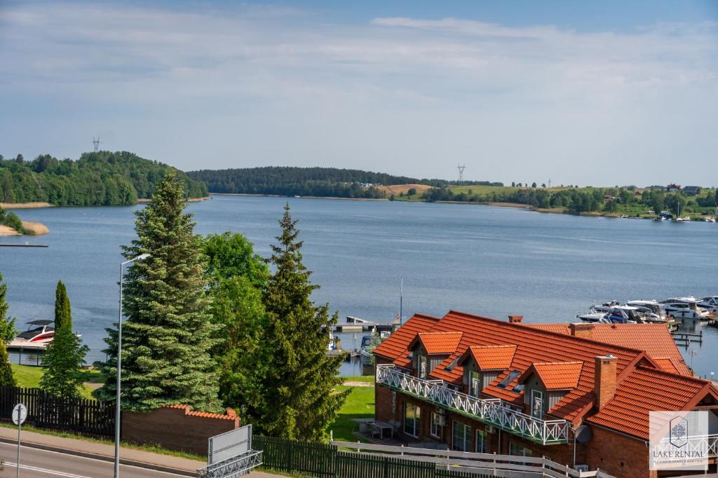 a building with an orange roof next to a body of water at Lake Rental P R A T U M 45 in Mikołajki