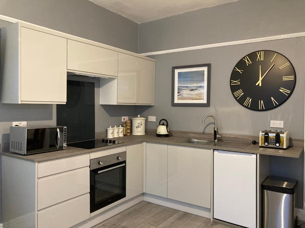 a kitchen with white cabinets and a clock on the wall at Beautiful holiday home near Plymouth for 4 in Plymouth
