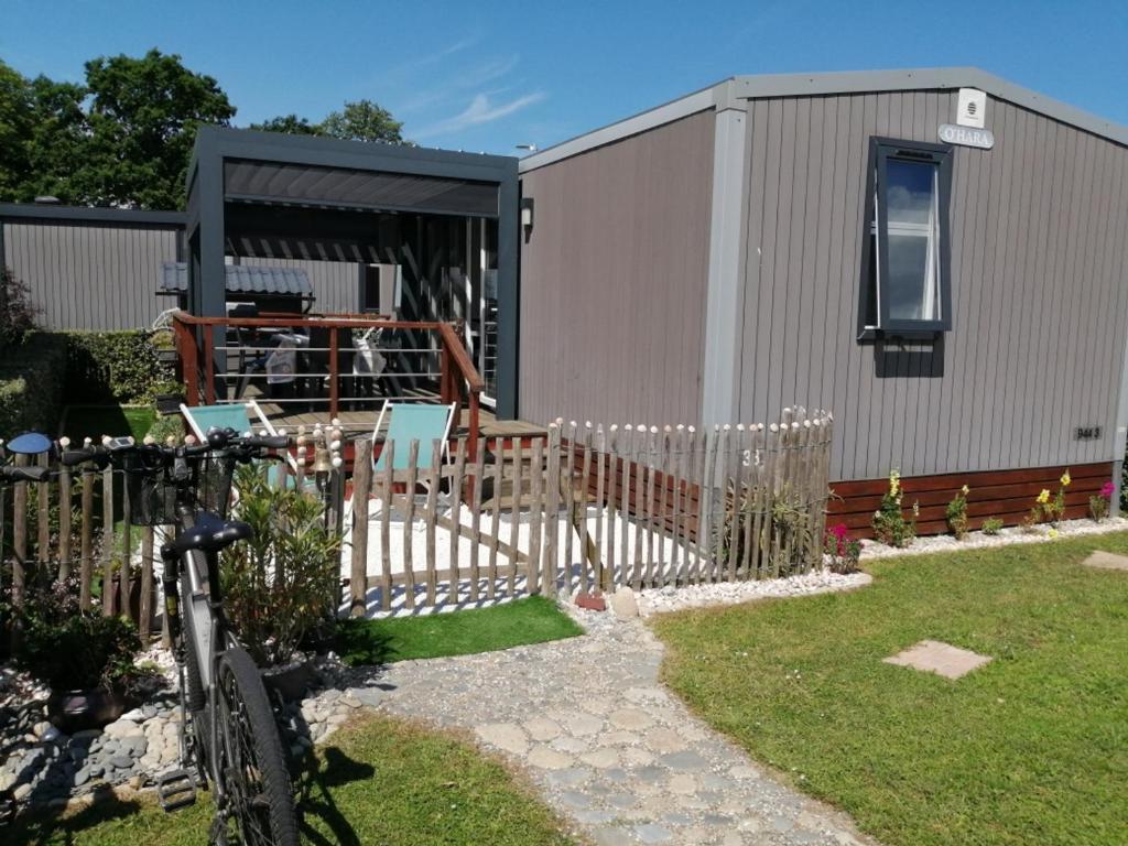 une maison avec une clôture et un vélo dans la cour dans l'établissement Mobil-home confort 3 ch, piscine chauffée, 200m plage, parking, WiFi, animaux admis - FR-1-361A-72, à Jullouville