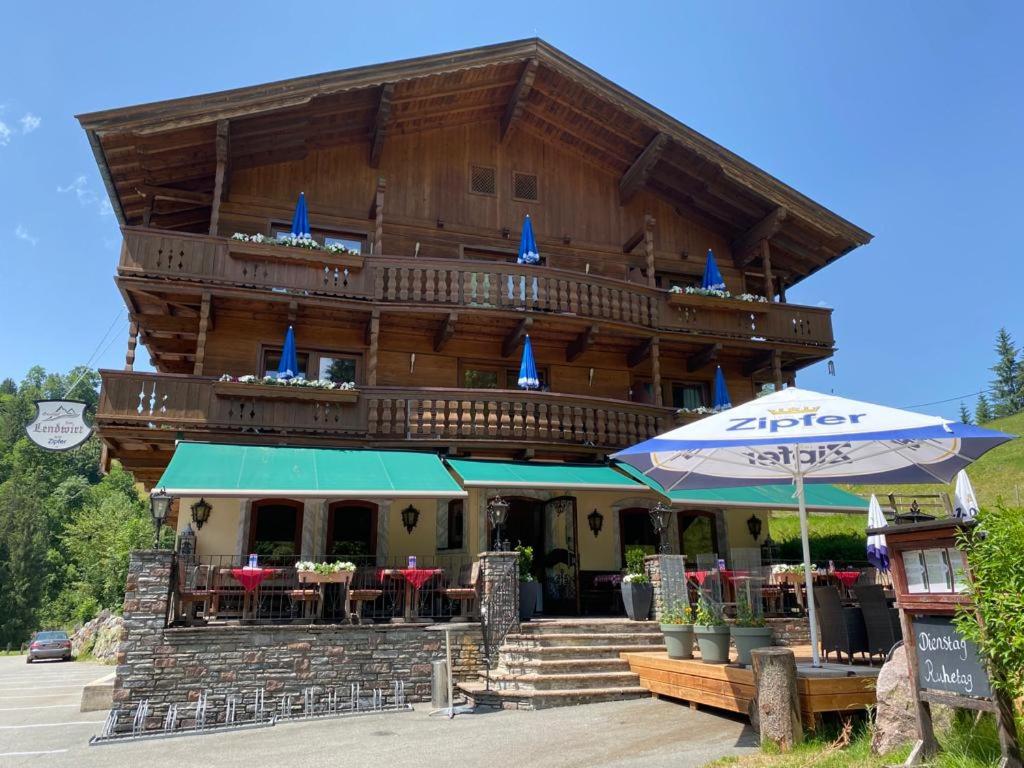 a large wooden building with tables and an umbrella at Gasthof Zum Lendwirt in Westendorf