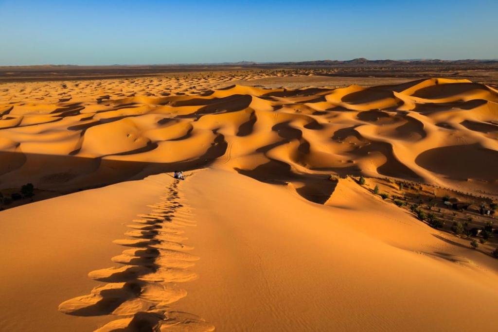 a person walking through a desert with footprints in the sand at Merzouga Camp Night in Merzouga